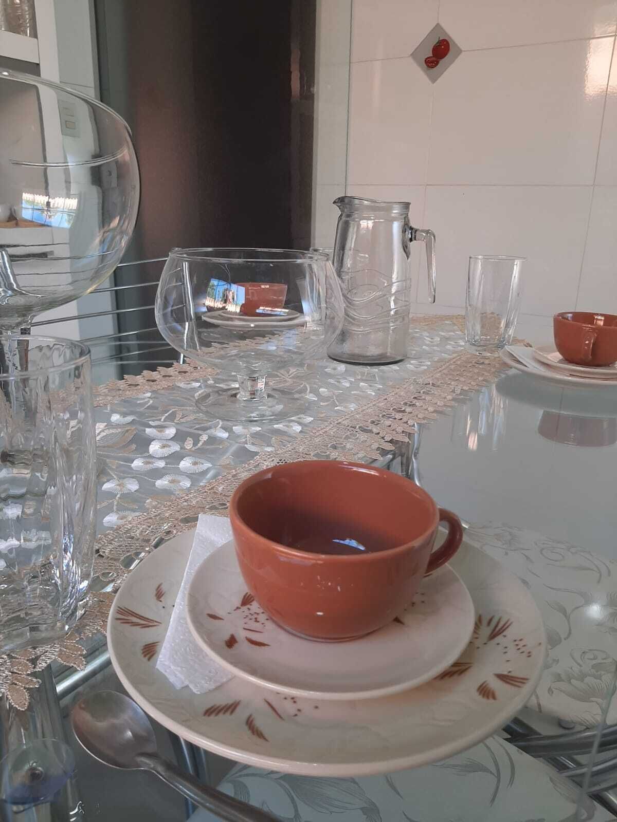 Una mesa de comedor con cristalería transparente, una taza roja y una jarra.