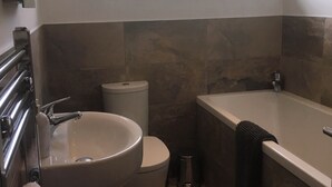 A bathroom with a large sink, toilet, and bathtub. There is a window providing natural light and a view of greenery outside.