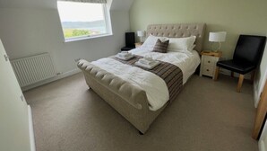 A bedroom with a large bed, a window, a chair, and a nightstand.