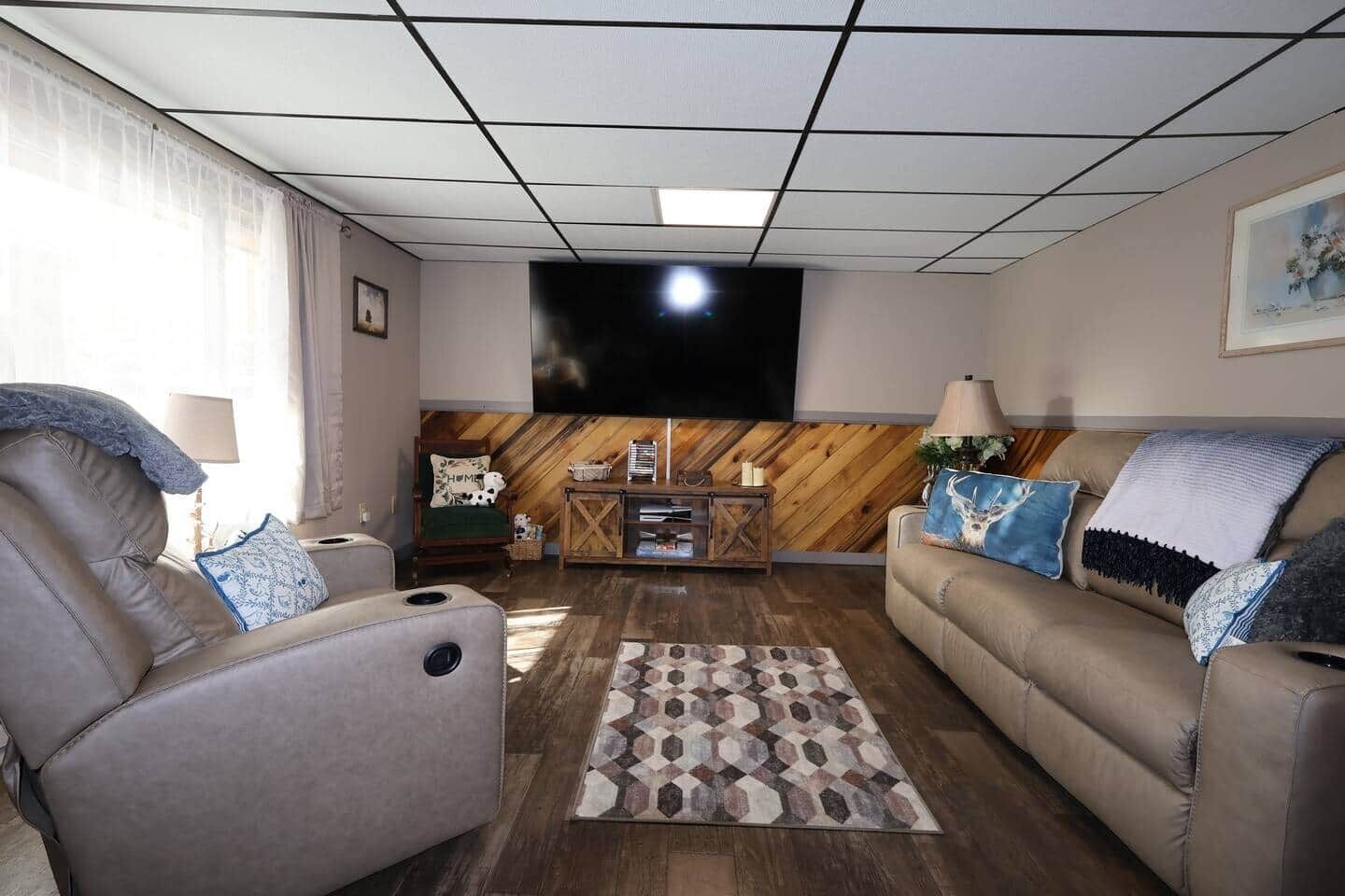 Uma sala de estar com sofá, poltrona, parede de destaque em madeira, televisão e tapete estampado.