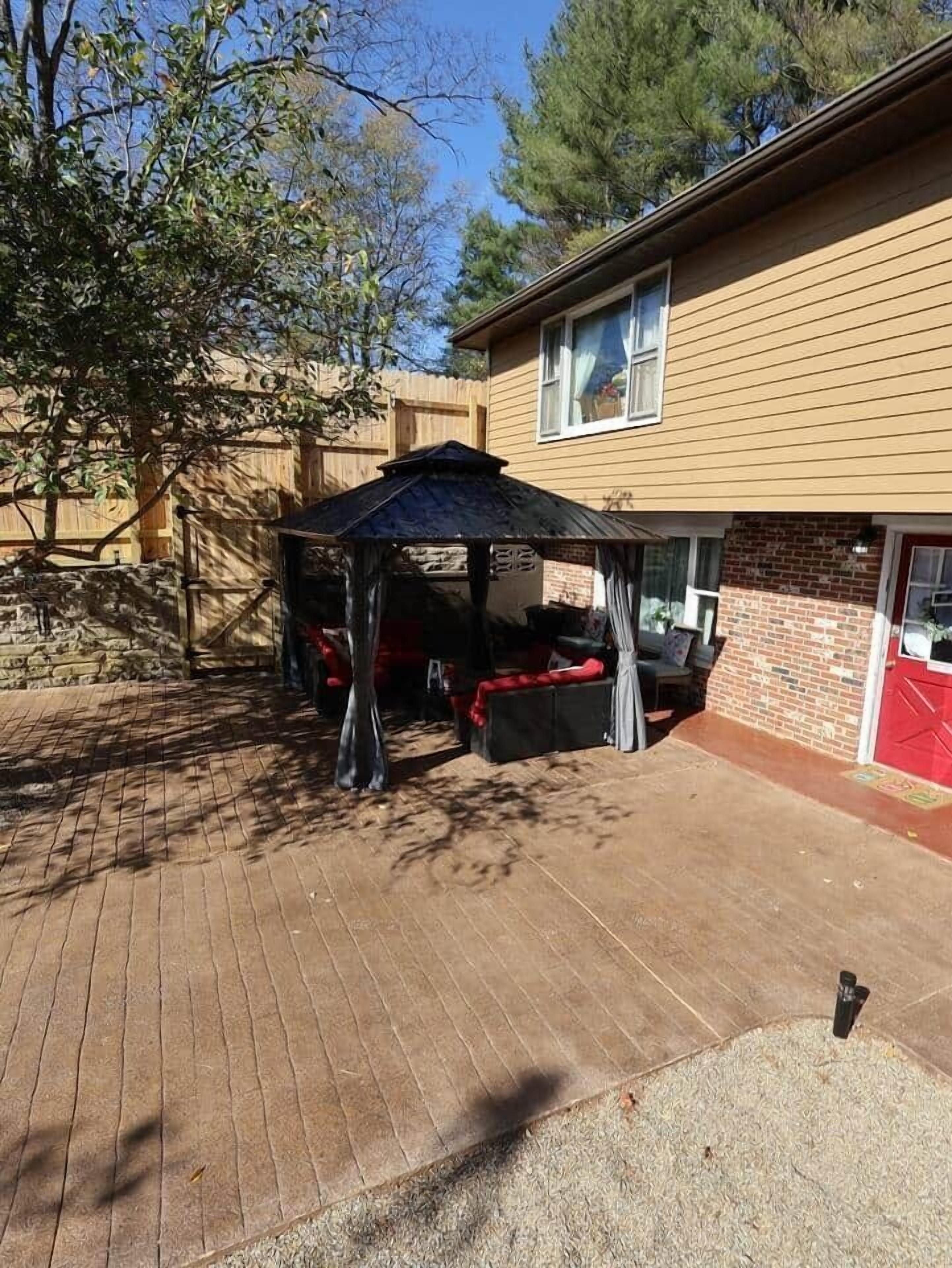 A backyard with a covered patio area, a brick patio, a stone wall, and a wooden fence.