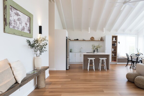 A modern kitchen with white cabinets and a central island, a dining area with a white table and chairs, and a bench with cushions. - Romantic Guest House with Mountain Views (Witheren)