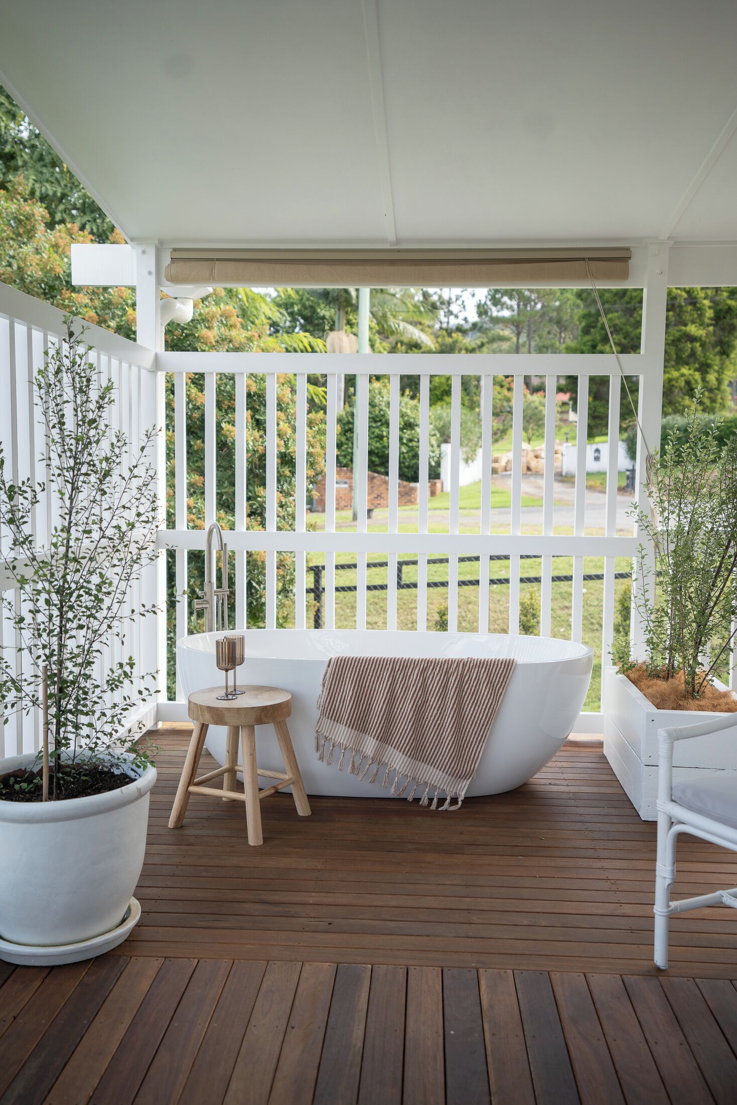 Une terrasse en bois avec une baignoire blanche, un petit tabouret et une plante en pot.