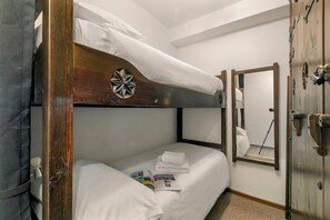 Ein Stockbett mit weißer Bettwäsche, ein kleiner Nachttisch mit Lampe und ein Spiegel an der Wand.