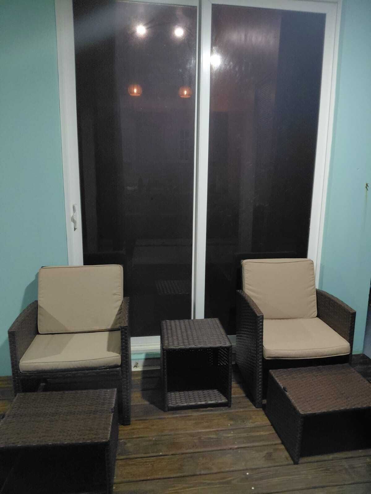 Un balcon avec deux fauteuils en osier et une petite table, une porte-fenêtre coulissante et un plancher en bois.