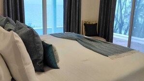 Ein Schlafzimmer mit einem großen Bett, dunklen Vorhängen und Blick ins Freie.