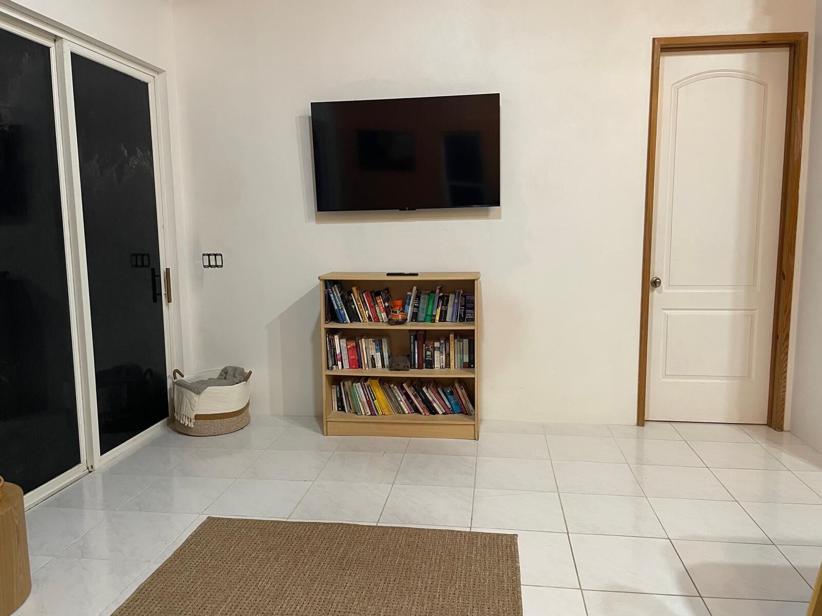 Una habitación con puerta corredera de vidrio, una estantería, un televisor montado en la pared y una puerta cerrada.