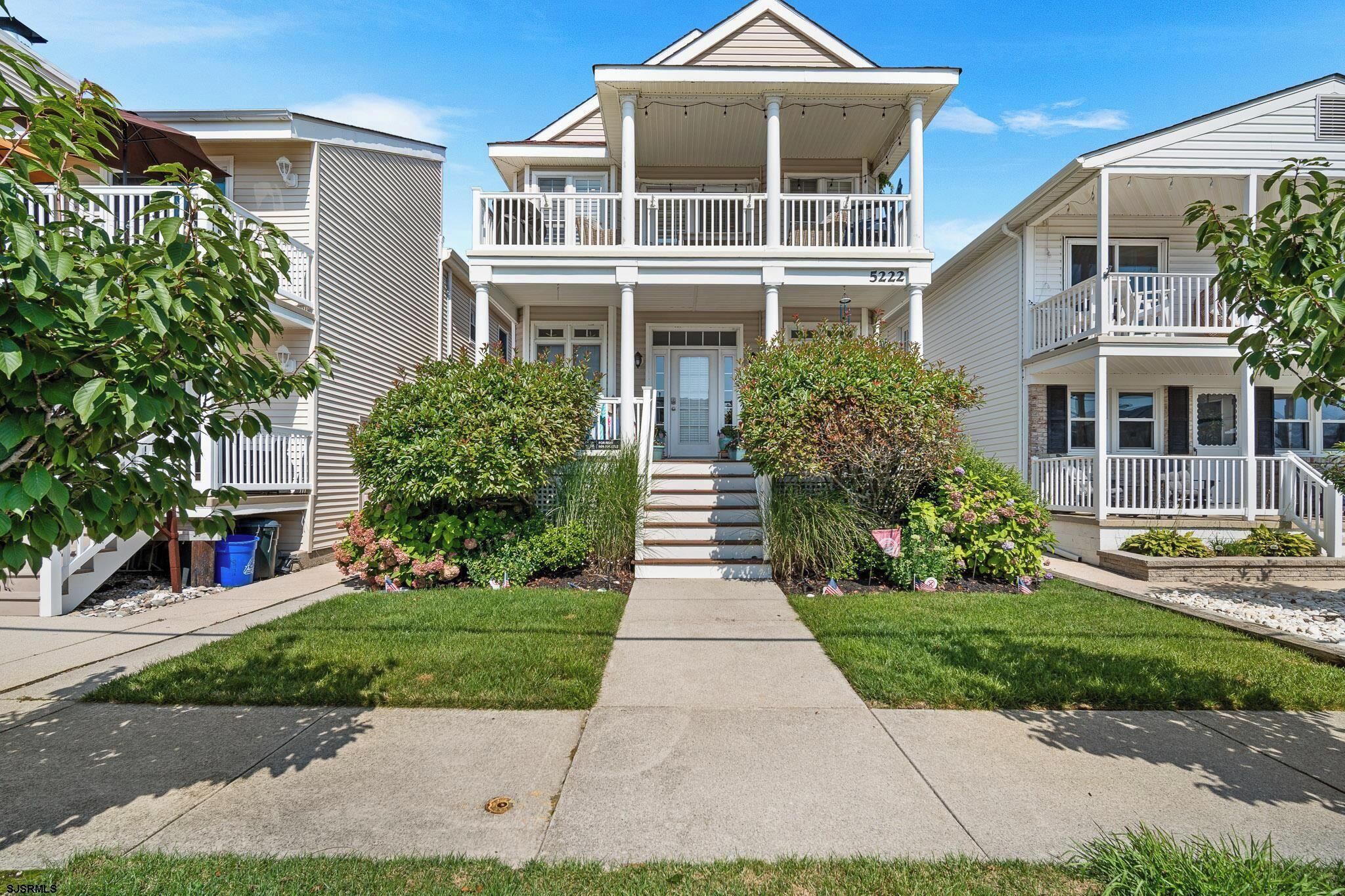 A two-story residential building with a front porch, a staircase leading to the entrance, and a well-maintained lawn.