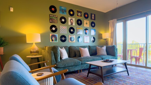 A living room with a green wall, a sofa, a coffee table, and a collection of vinyl records on the wall. - Retro 1 Bedroom, King Bed, Large Living Area, Parking, Gym, Close to UAB (Birmingham)