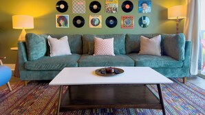 A living room with a green sofa, a white coffee table, and a wall decorated with vinyl records. - Retro 1 Bedroom, King Bed, Large Living Area, Parking, Gym, Close to UAB (Birmingham)