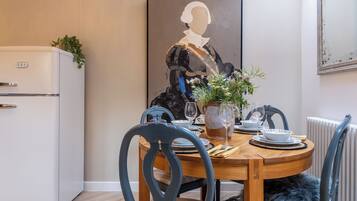 Un coin repas avec un réfrigérateur blanc, une table en bois mise pour le repas et un tableau accroché au mur.