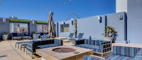 A rooftop lounge with outdoor seating, string lights, and a fire pit.