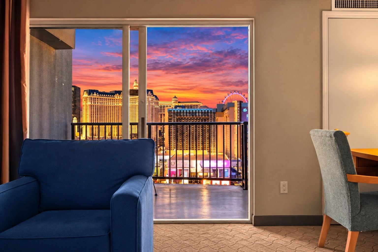 Ein Zimmer mit Blick auf eine Skyline bei Sonnenuntergang, ein blaues Sofa und ein Holzsessel.