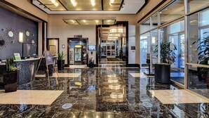 Vestíbulo de hotel con piso de mármol, mostrador de recepción y puerta de vidrio que da al acceso.