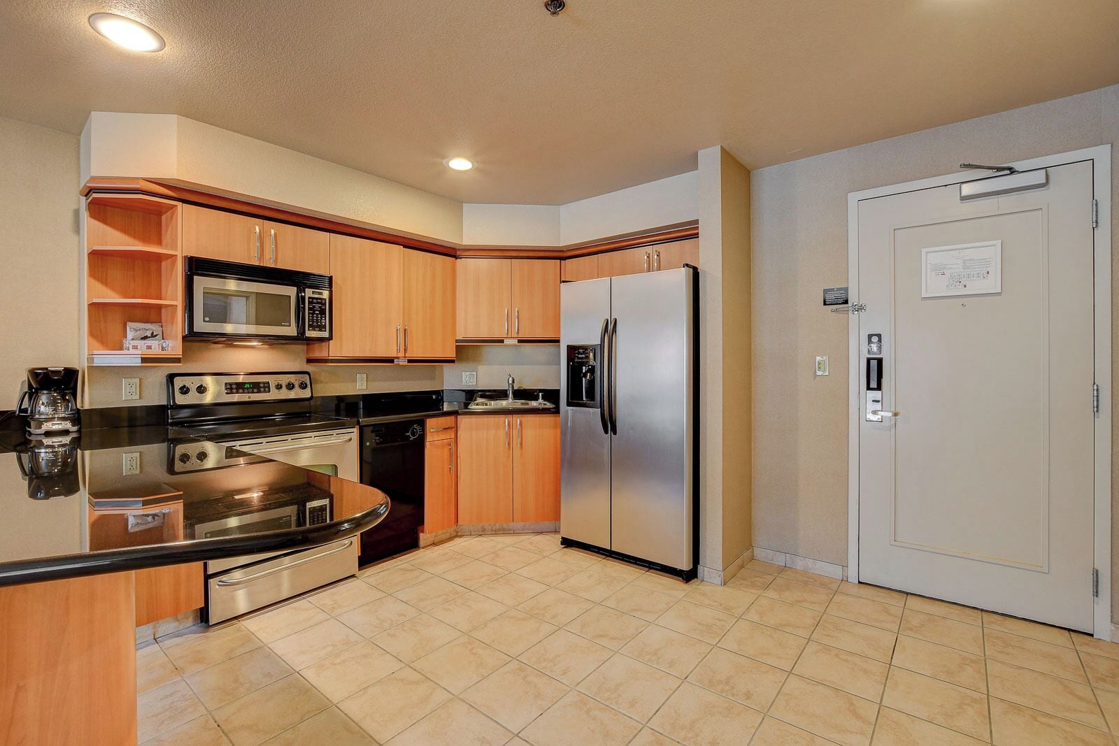 A modern kitchen with stainless steel appliances, wooden cabinets, and a tiled floor.