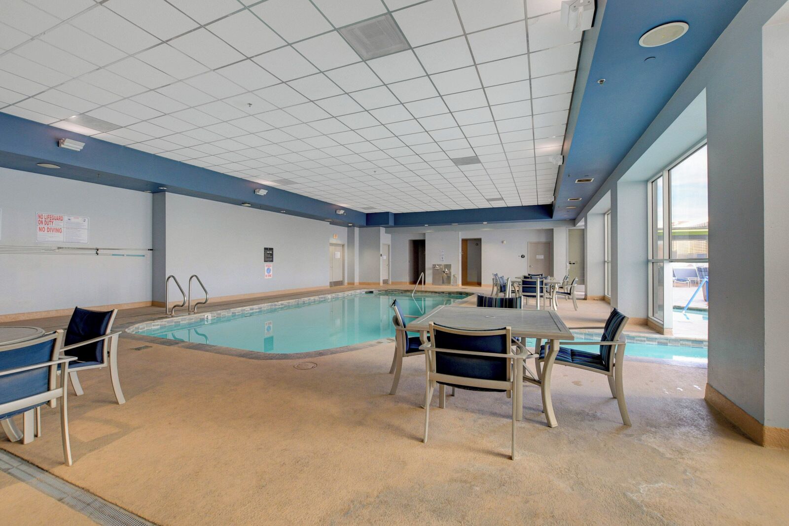 Un espace piscine doté d’un plafond carrelé, d’une piscine et de sièges disposés autour de celle-ci.