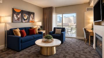 Habitación de hotel moderna con un sofá azul, una mesa de centro redonda y vistas a la ciudad desde el balcón.