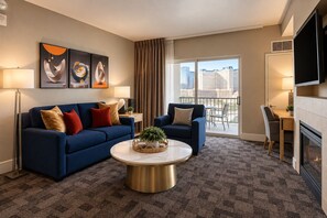 Une chambre d’hôtel moderne avec un canapé bleu, une table basse ronde et une vue sur la ville depuis le balcon.