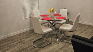 Een eetgedeelte met een ronde glazen tafel, vier witte stoelen met kussens en een decoratief middelpunt.