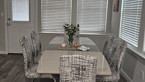 Ein Essbereich mit einem rechteckigen Tisch, vier Stühlen und einem Fenster mit Jalousien.