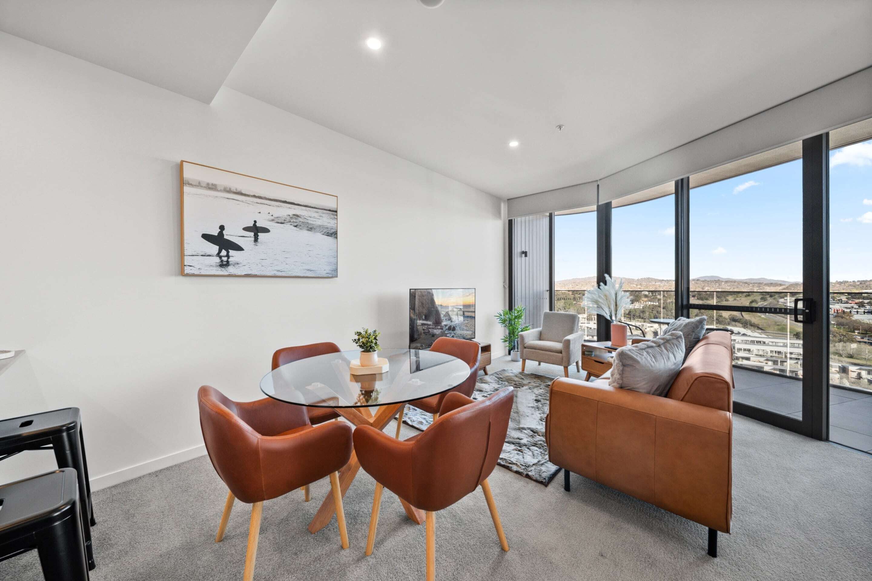 A modern living room with a glass table, leather chairs, a sofa, and a large window with a city view.