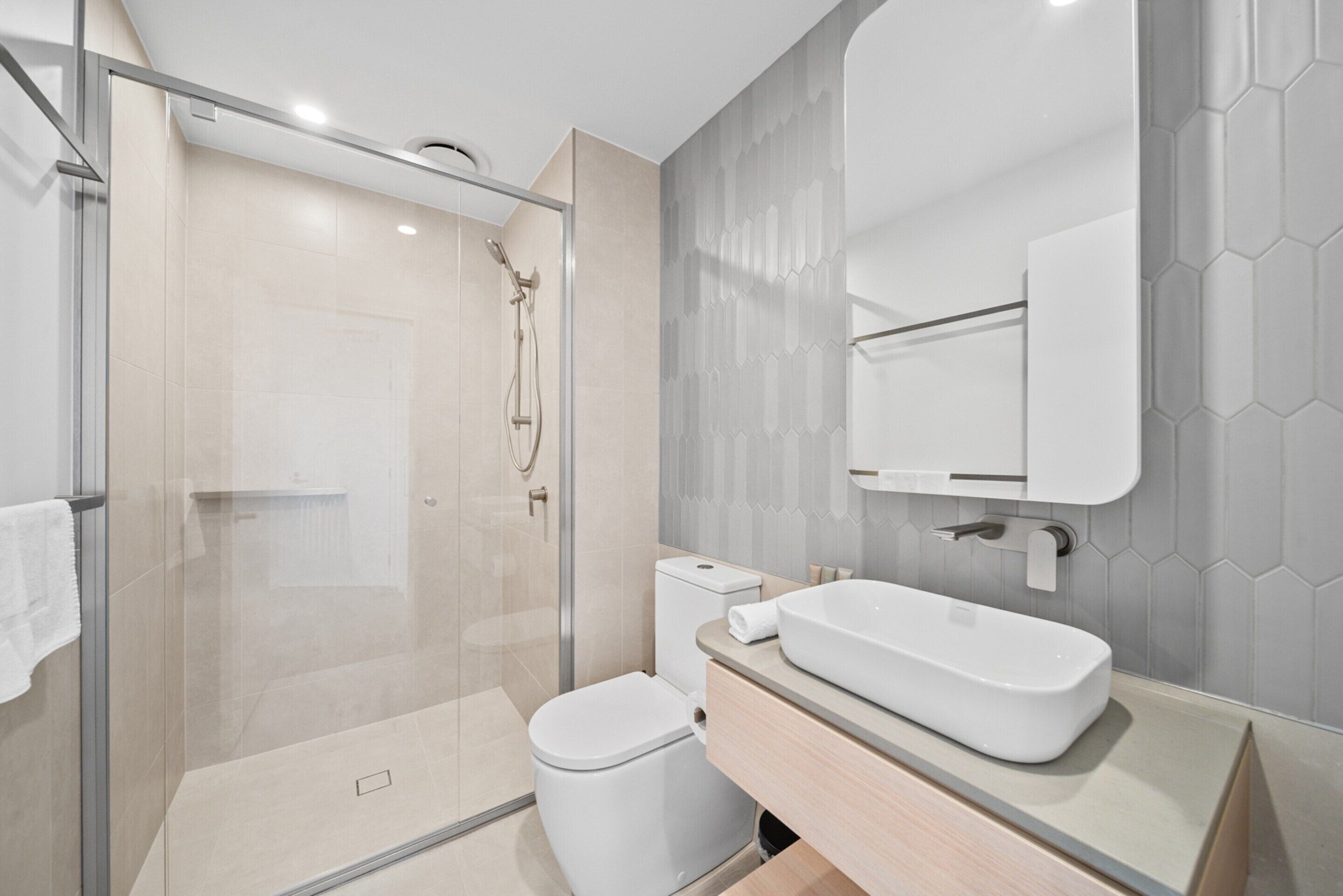 Een moderne badkamer met een douchecabine van glas, een wit toilet en een groot rechthoekig wastafel.