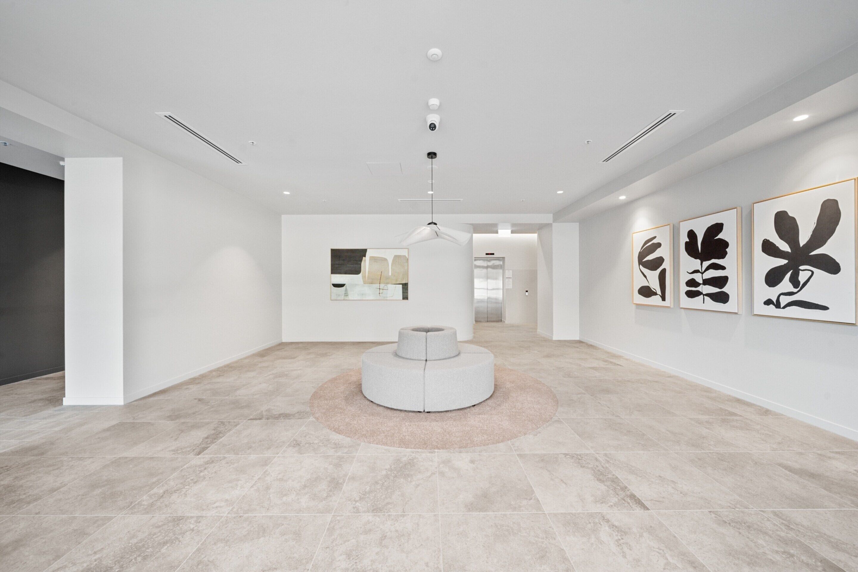 A modern, minimalist hotel lobby with a central seating area, a large mirror, and abstract art on the walls.