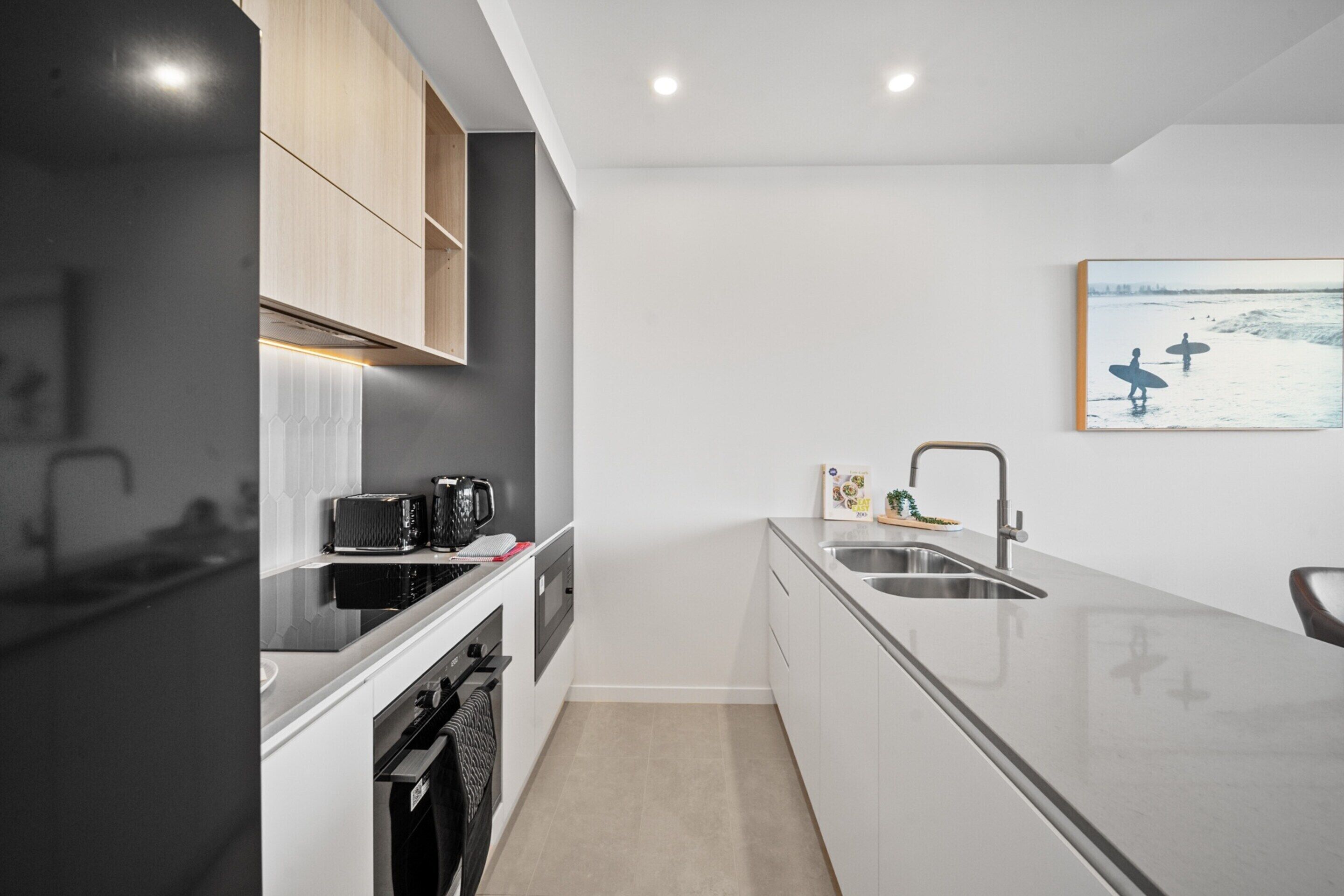 Una cocina moderna con armarios blancos, una estufa negra y un lavamanos de acero inoxidable.