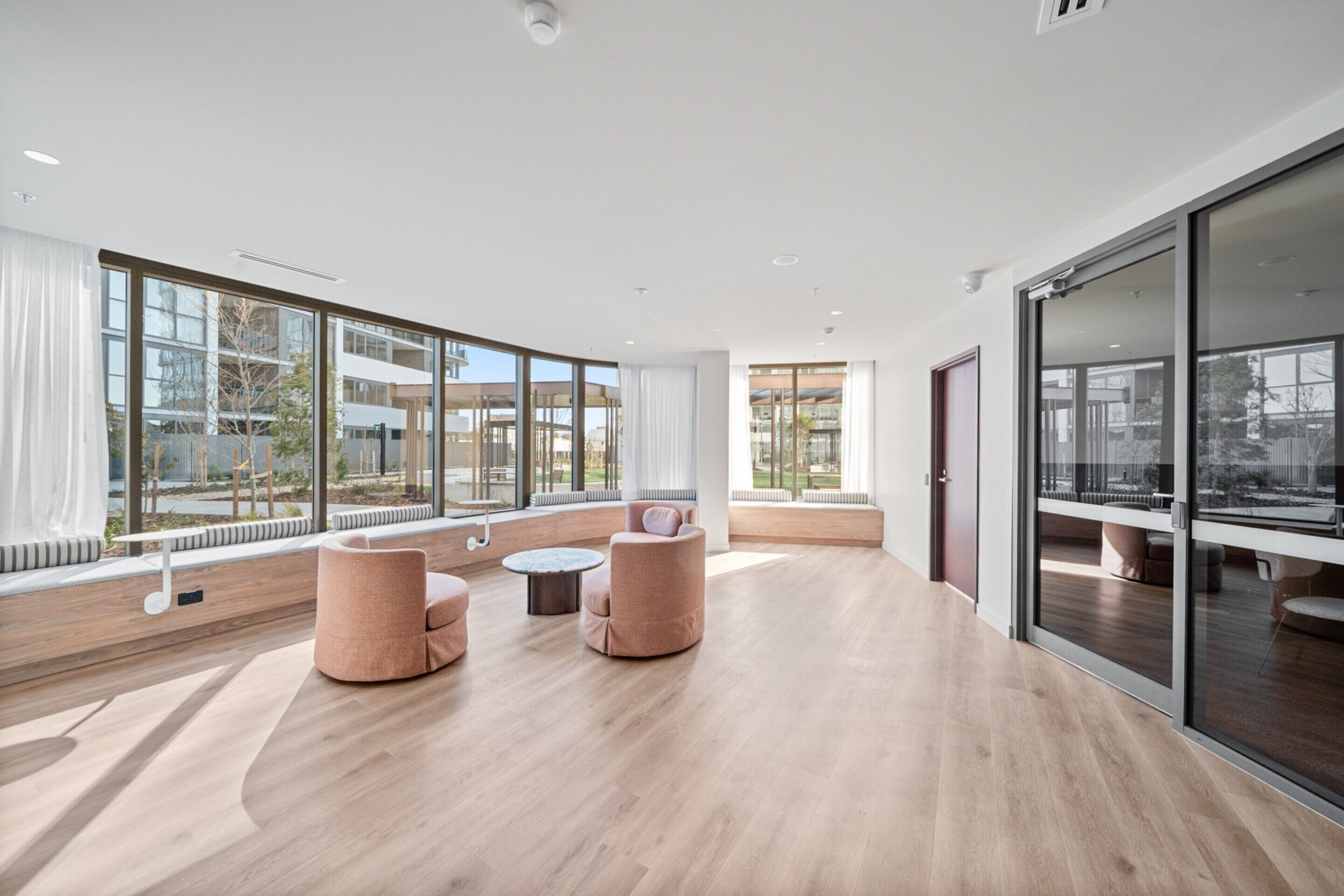 A spacious room with large windows, a wooden floor, and a seating area with two sofas and a small table.