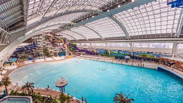 En inomhusbadpark med en stor pool, vattenrutschkanor och ett avskärmat område med sittplatser.