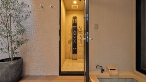 Un bagno moderno con porta in vetro, una panca in legno e una pianta in vaso.