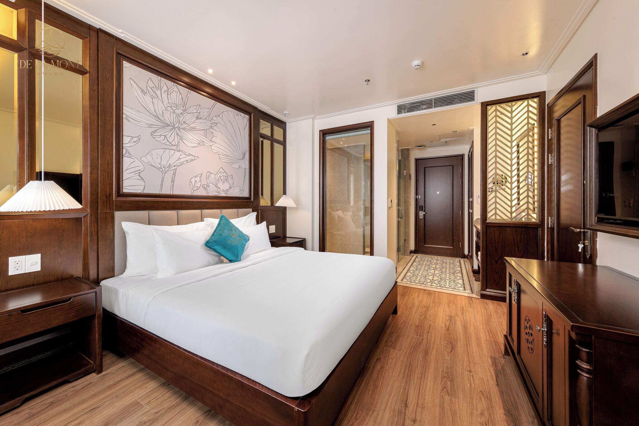 A hotel room with a large bed, wooden headboard, a wall-mounted artwork, a television, and a wardrobe.