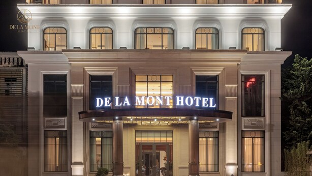 Das De La Mont Hotel mit einer prunkvollen Fassade, großen Fenstern und beleuchteter Beschilderung.