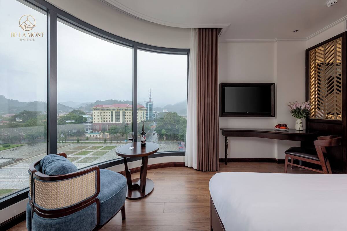 Une chambre d’hôtel dotée d’un mur en verre incurvé, d’un lit, d’un bureau, d’une chaise et d’un téléviseur.
