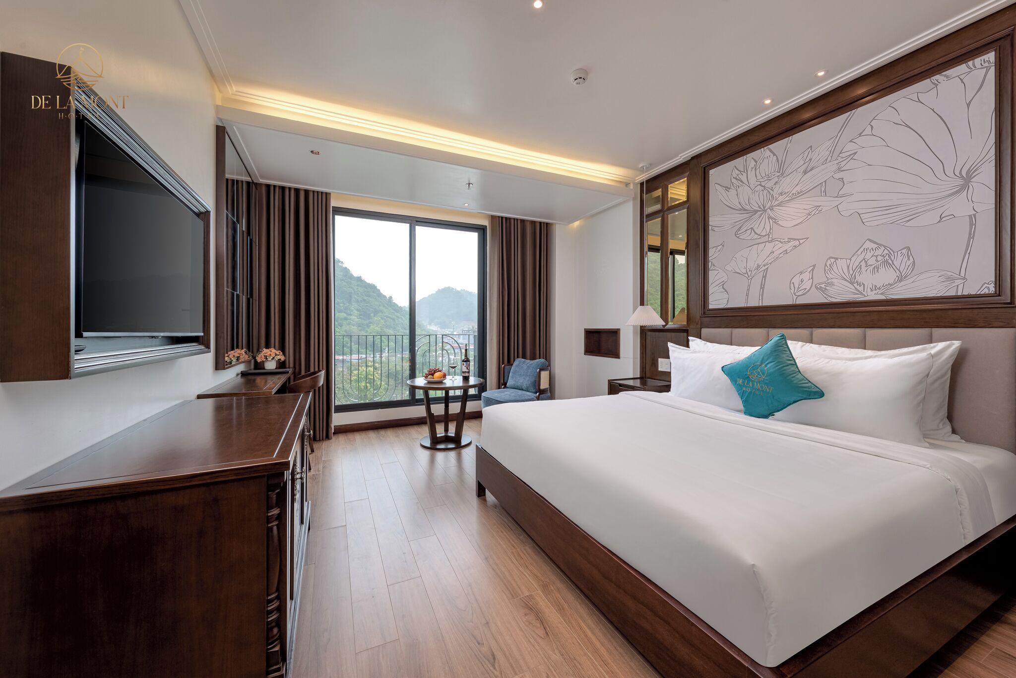 Habitación de hotel con una cama grande, televisión, escritorio, una pequeña mesa con fruta, una silla y vistas a las montañas a través de la ventana.
