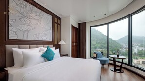 Ein Hotelzimmer mit einem großen Bett, Blick auf einen Berg und einem kleinen Tisch mit einer Weinflasche.