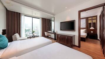 Habitación de hotel con dos camas, un escritorio, una silla, un televisor y un balcón con cortinas.