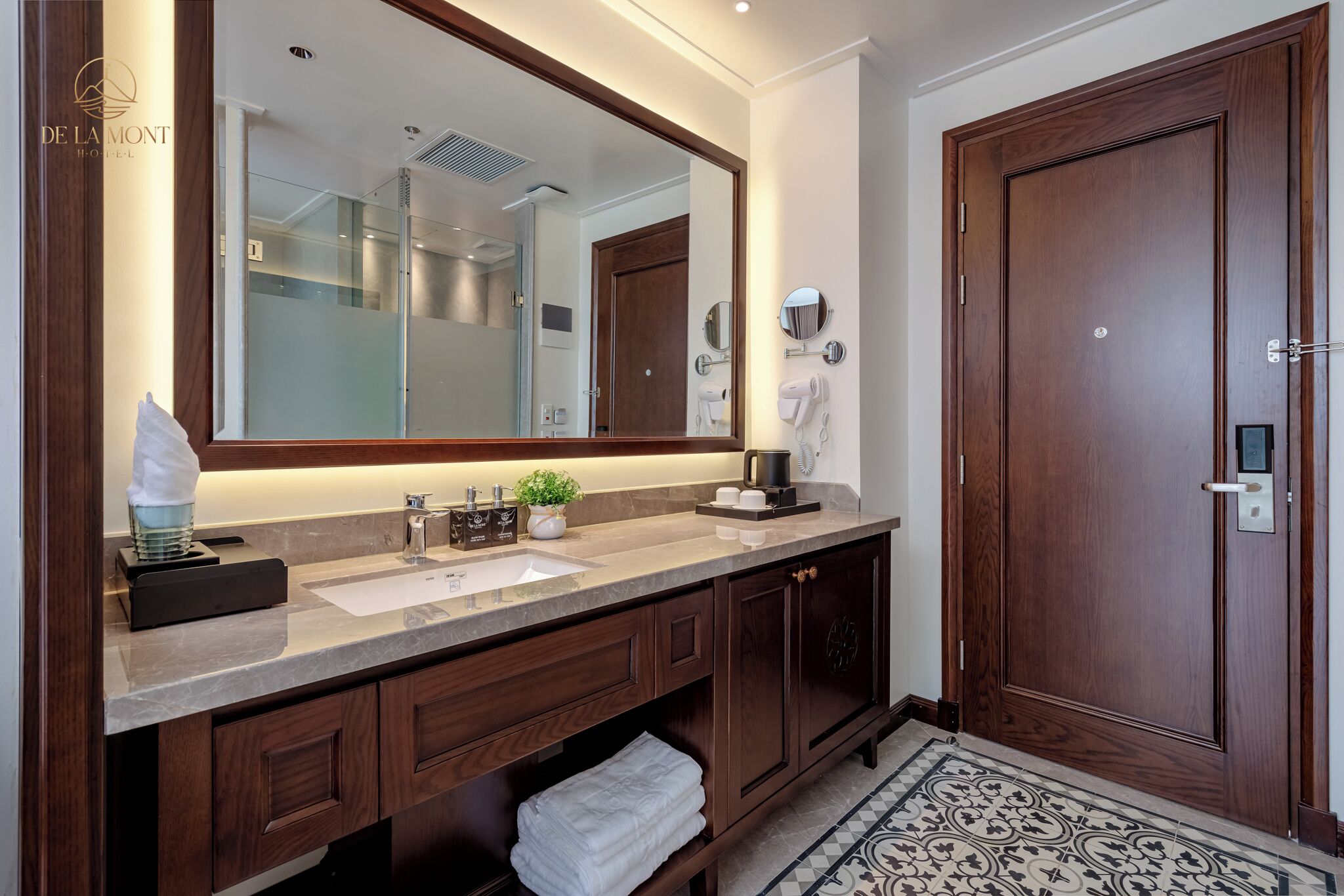 Une salle de bain d’hôtel avec un grand miroir, des meubles en bois, un lavabo et un porte-serviettes.