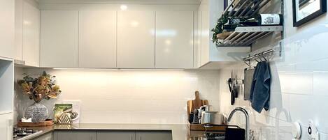 A modern kitchen with white cabinets, a stainless steel sink, and a wooden floor.