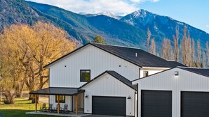 Een modern huis met twee verdiepingen, een garage, een overdekt terras en een berg op de achtergrond.