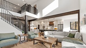 Een ruime woonkamer met een hoge plafond, een trap en een keuken op de achtergrond.
