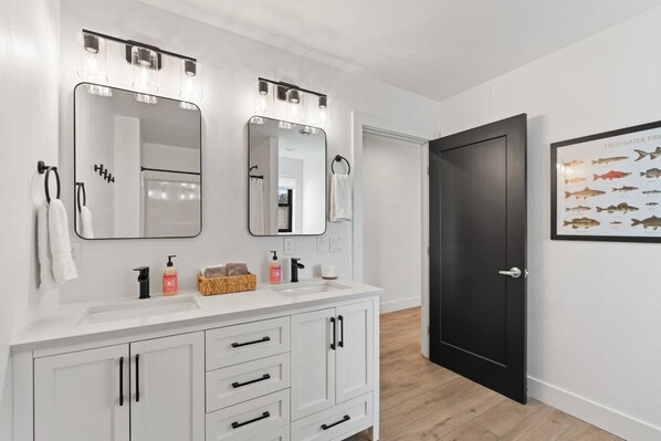 A modern bathroom with two mirrors, a white vanity, and a black door.