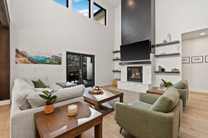 A spacious living room with a fireplace, a large TV, and a view of the outdoors.