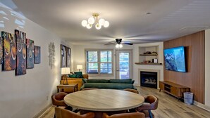 A modern living room with a round wooden dining table, comfortable seating, a fireplace, and a large flat-screen TV mounted on the wall. - Downtown Helen - 1st Floor | Free Parking (Helen)