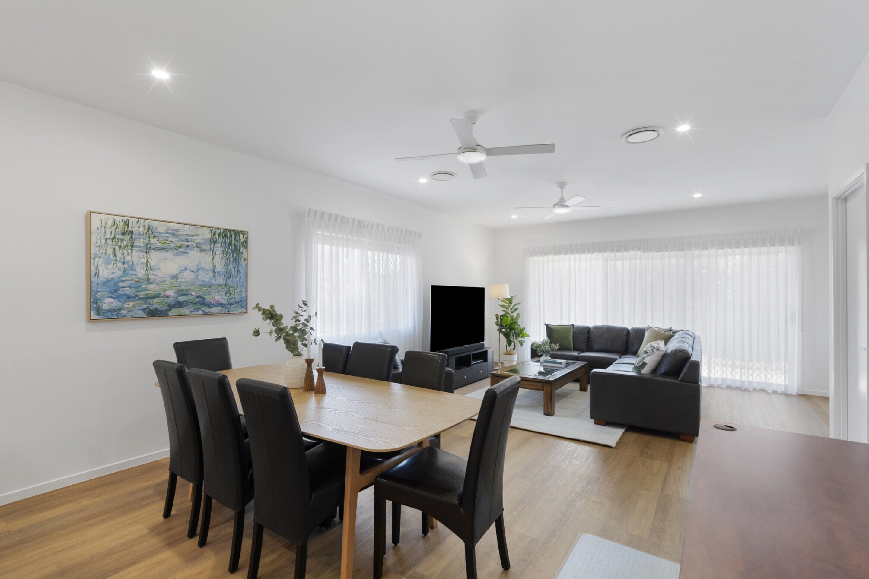 A modern living room with a dining area, featuring a flat-screen TV, a sofa, and a coffee table.