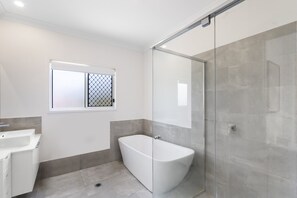 Un baño moderno con una bañera independiente, una cabina de ducha de vidrio y un ventanal con celosía metálica.