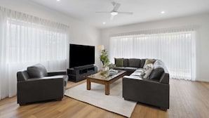 Una sala de estar moderna con un televisor de pantalla plana, dos sofás, una mesa de centro y un ventilador de techo.