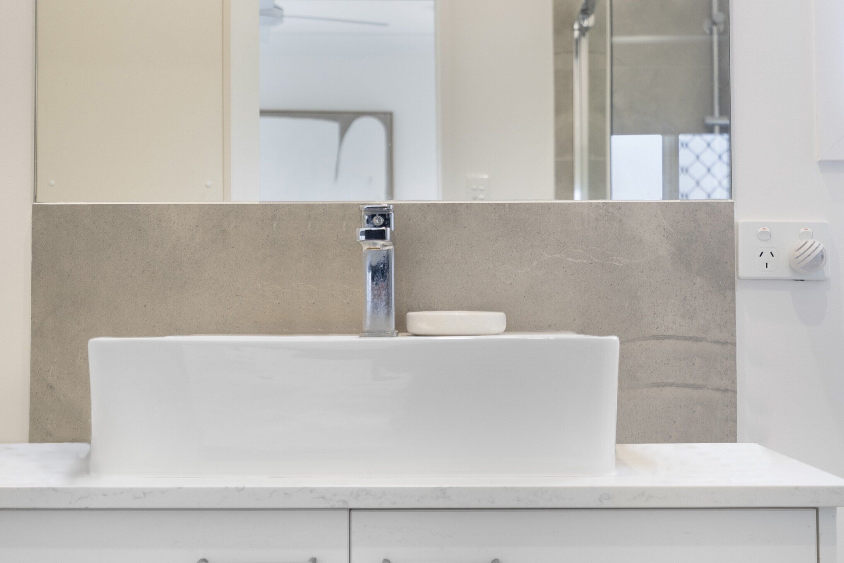 Une salle de bain avec un lavabo blanc, un miroir et un mur de couleur beige.