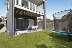 Una casa de dos pisos con un balcón, un trampolín y un patio con mesa y sillas.