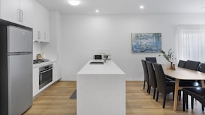 Una cocina moderna con armarios blancos, una isla central y un comedor con mesa y sillas de madera.